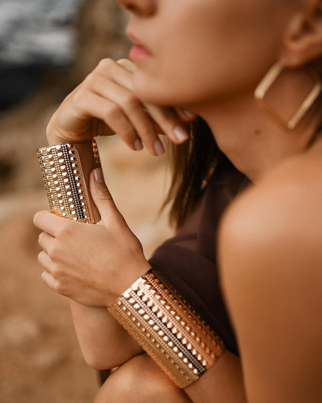 Close-up of a woman's hands and gold jewelry against the natural rock textures at Cala Moraig.