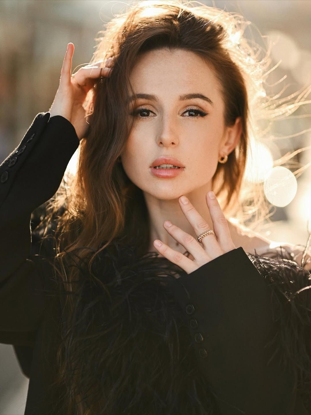 An elegant close-up portrait of a woman in a feather top, perfectly lit by soft golden sunlight for a high-fashion look.