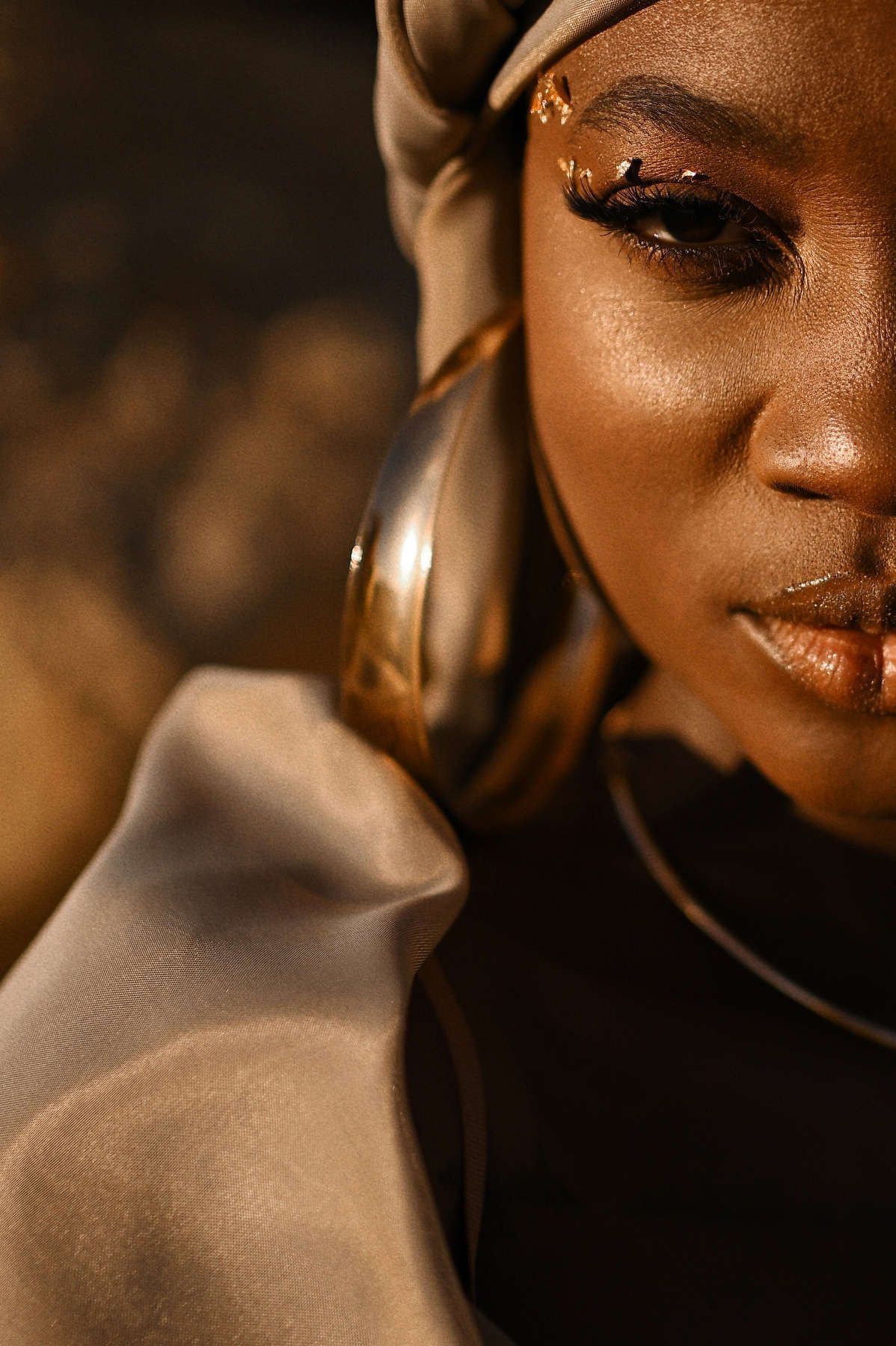 Professional fashion beauty portrait featuring detailed gold makeup and statement jewelry for commercial brand campaigns.