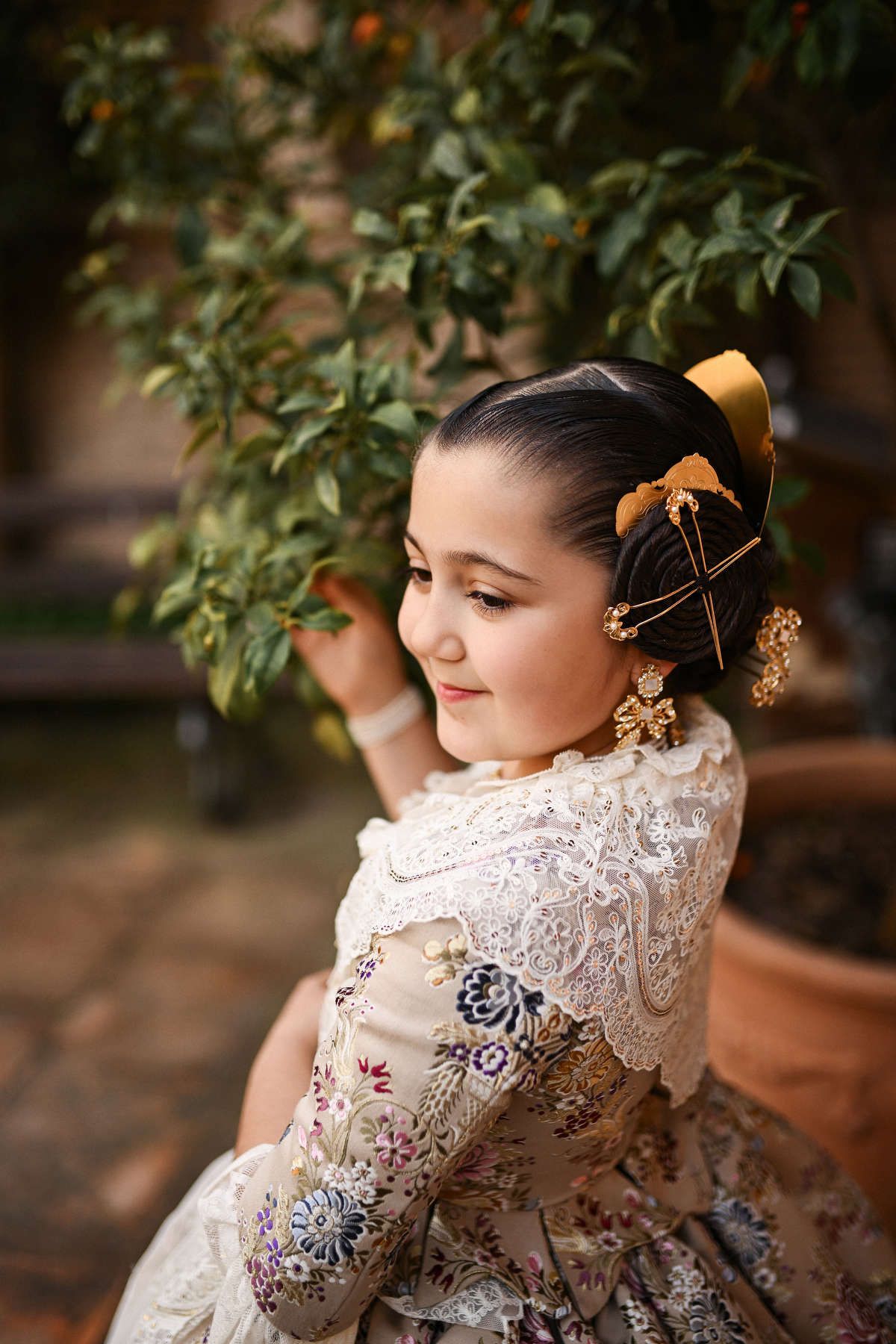 A side-profile portrait of a young girl in a traditional Fallera costume, looking thoughtfully at plant in the neoclassical Monforte garden