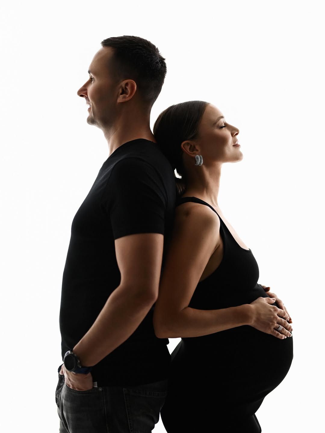 A stunning black and white silhouette portrait of an expectant couple standing back-to-back in a studio setting