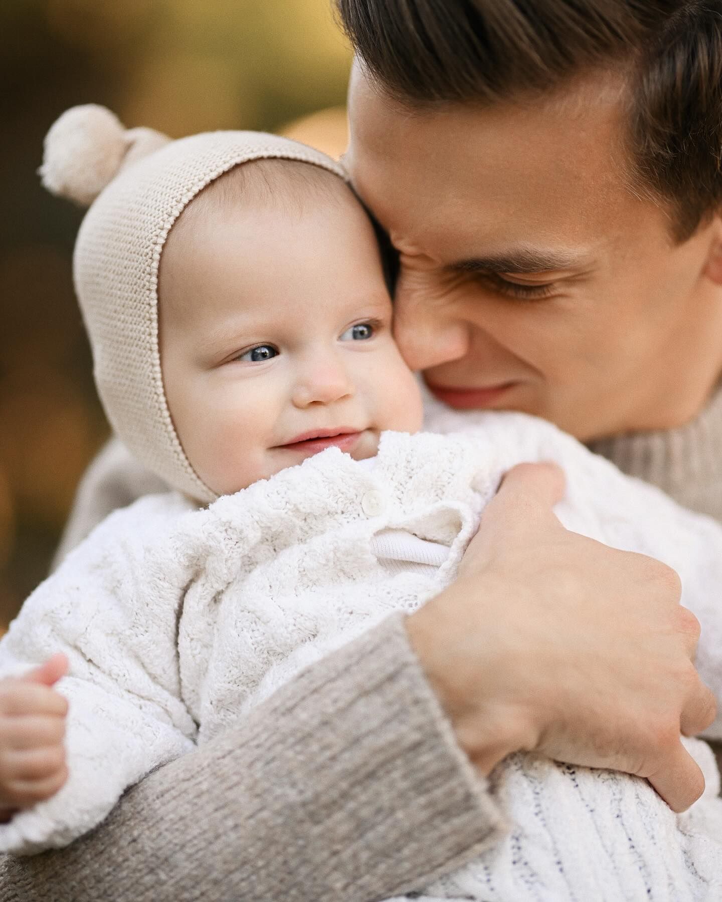 Close-up of a loving father gently embracing his small baby in a knit hat during a family portrait session in Turia Gardens.