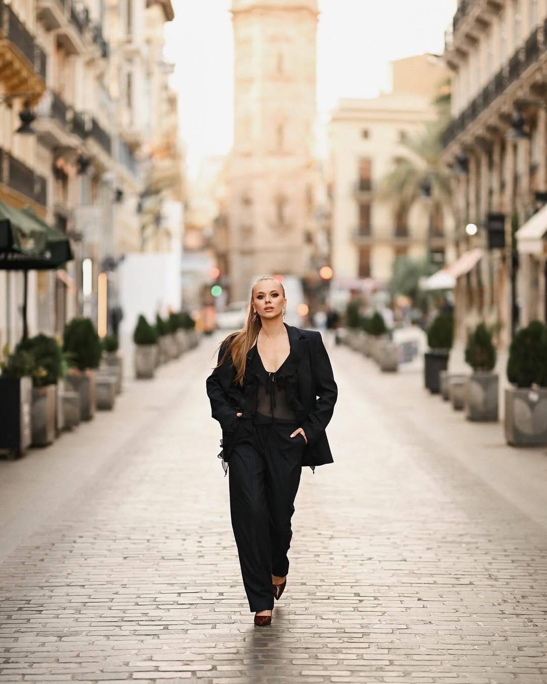 A powerful wide shot of a model walking towards the camera on a cobblestone street, exemplifying top-tier urban fashion photography.