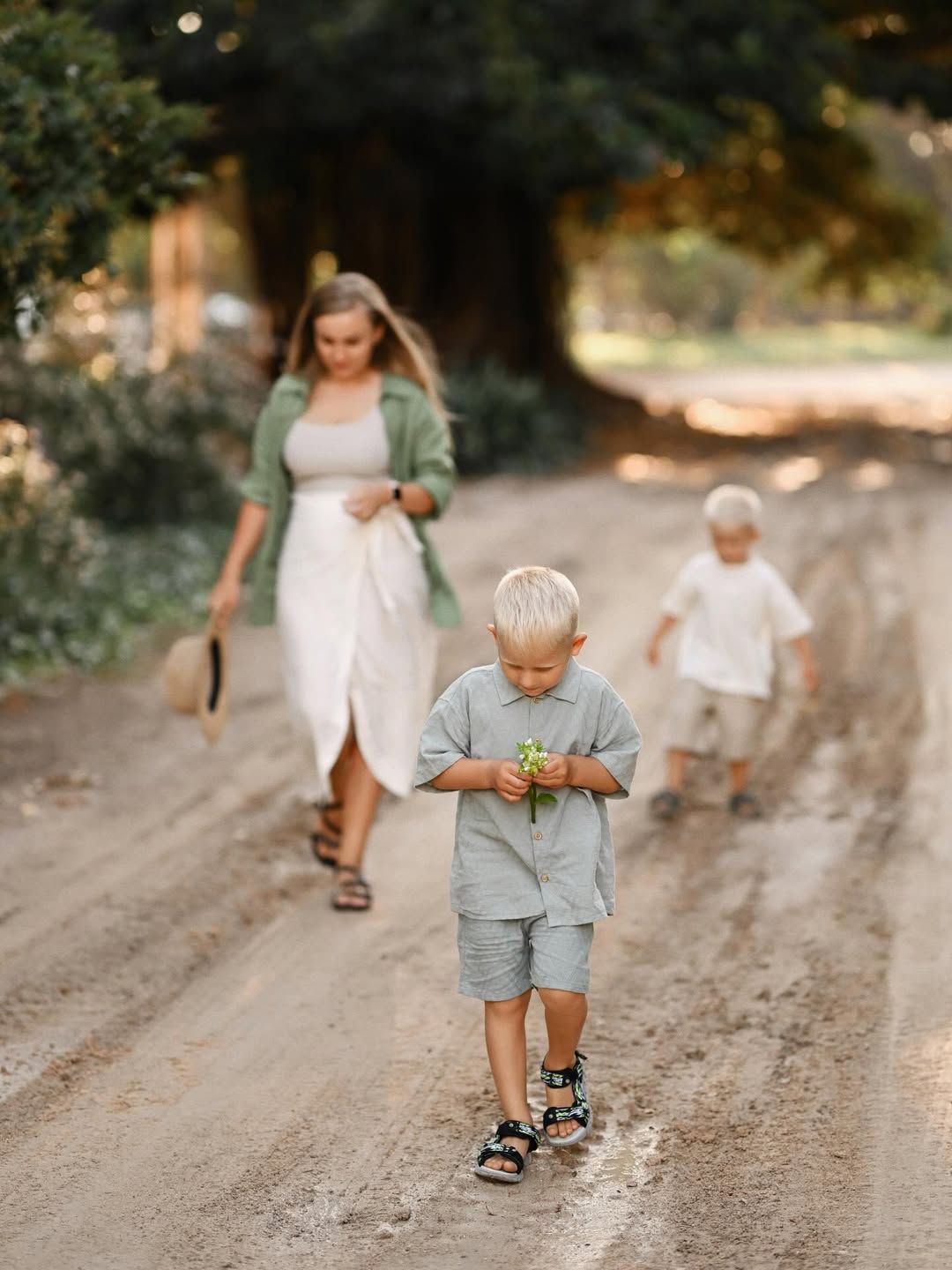 Two young brothers walking along a dirt path in Turia Park, Valencia while their parents follow behind.