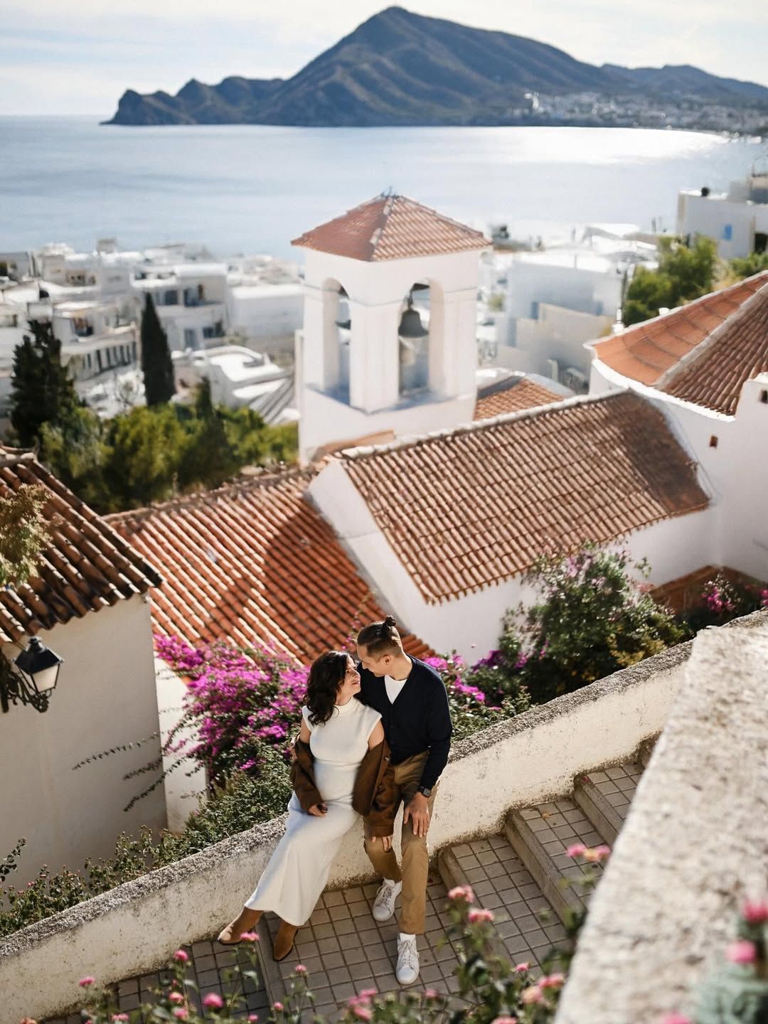 A couple sharing a romantic moment on a stepped path overlooking the white houses, church bell tower, and sea during an Altea love story.