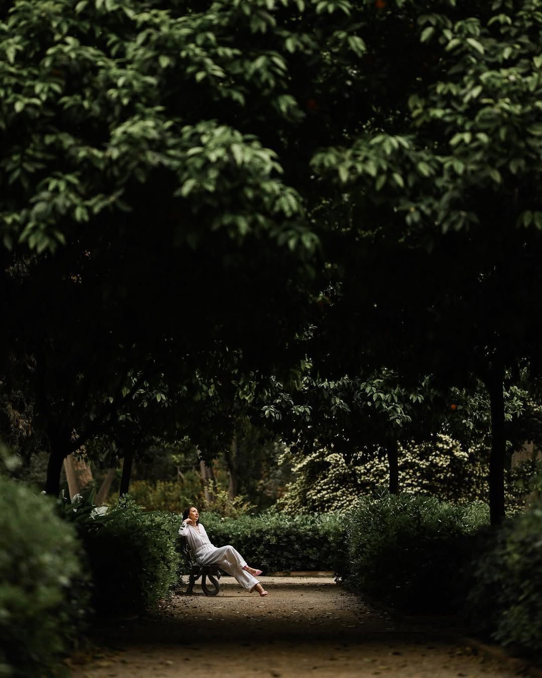 A distant view of a woman relaxing on a bench under a dense canopy of orange trees in Valencia.