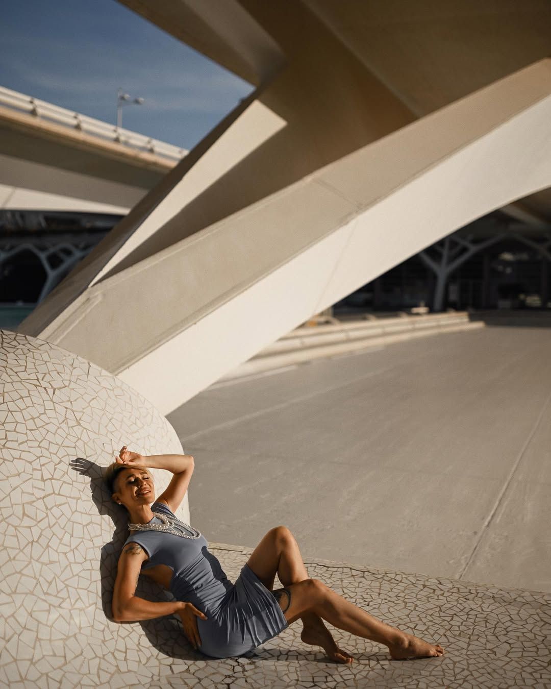 A woman in a blue dress posing dynamically against the futuristic white structures of the City of Arts and Sciences
