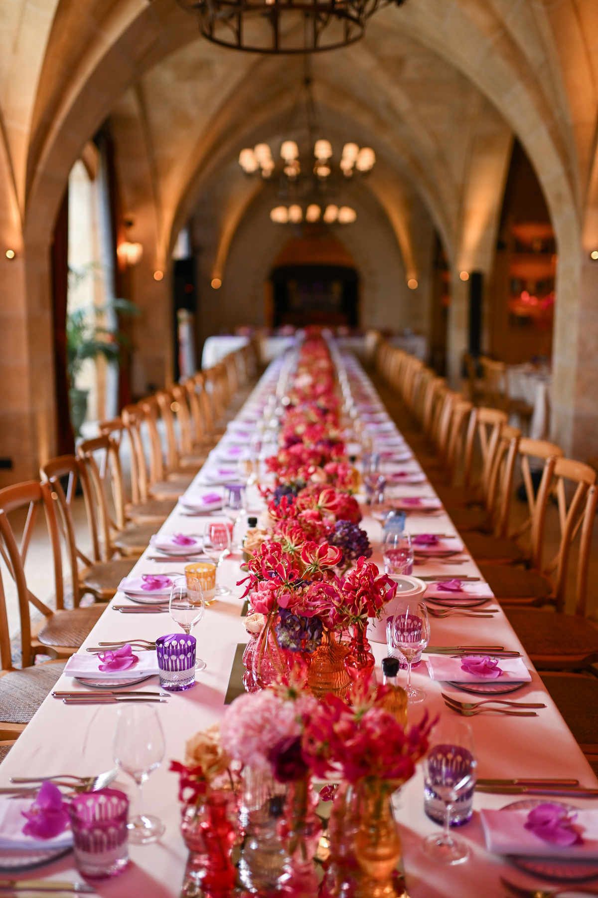 Chic indoor party banquet table decorated with delicate pink roses, tall candles, and dark green velvet chairs.