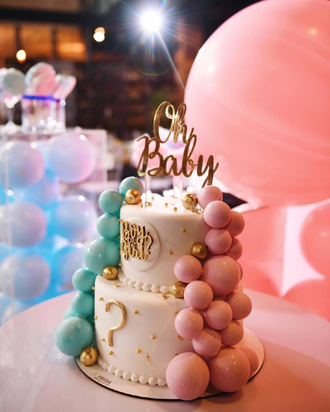 Close up of a beautiful two-tier Oh Baby gender reveal cake decorated with pink and blue spheres at an indoor venue in Valencia.