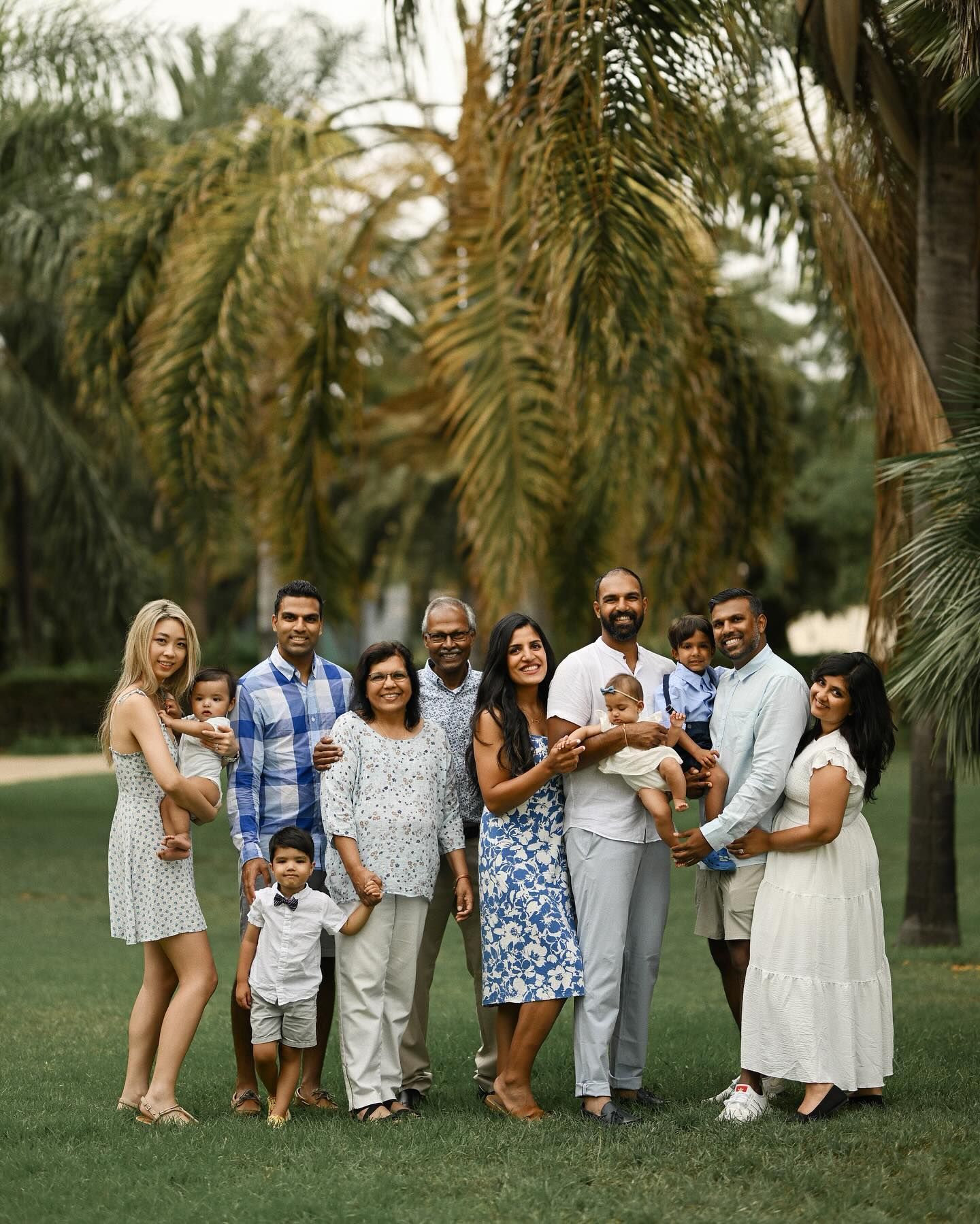 A multi-generational family posing together in a lush park with palm trees, capturing a joyful and timeless group portrait for the album.