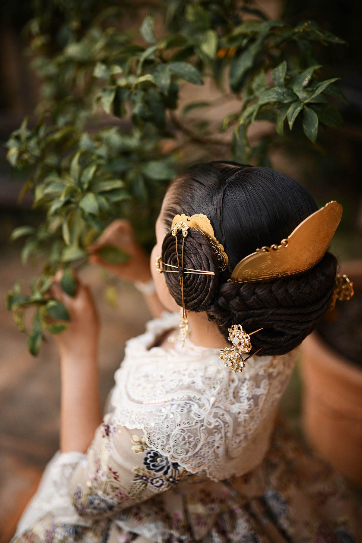 A detailed macro shot from above, showcasing the elaborate Fallera hair buns, golden peinetas, and ornate jewelry worn by the young girl.