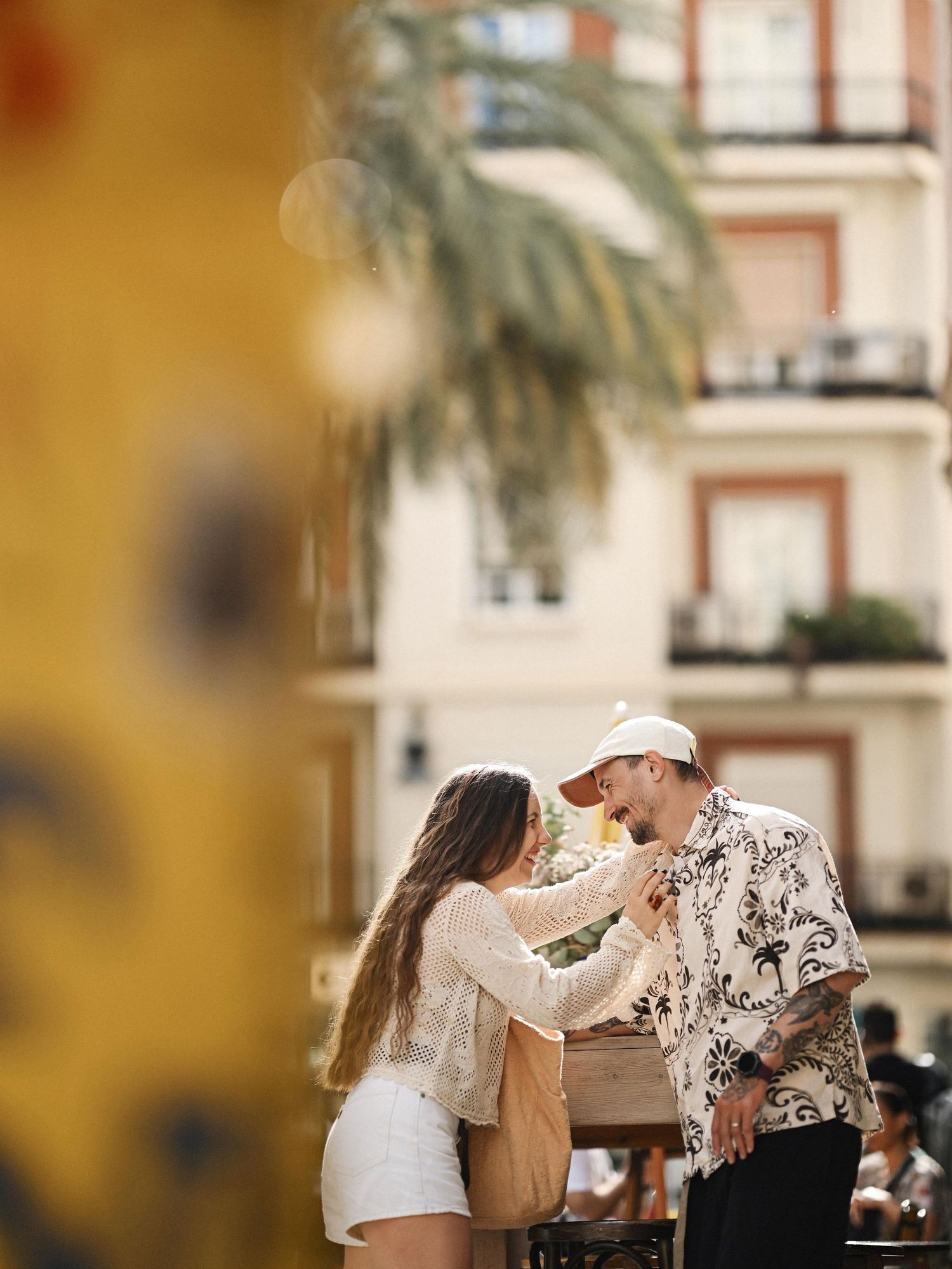 A smiling couple talking closely next to an outdoor cafe counter in the sunlit historic streets of Valencia city centre.