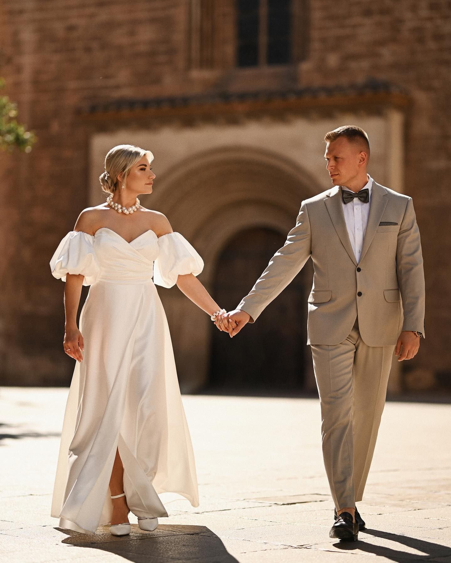 Bride and groom walking hand in hand past the grand civic buildings and golden stone architecture during their Valencia city elopement.
