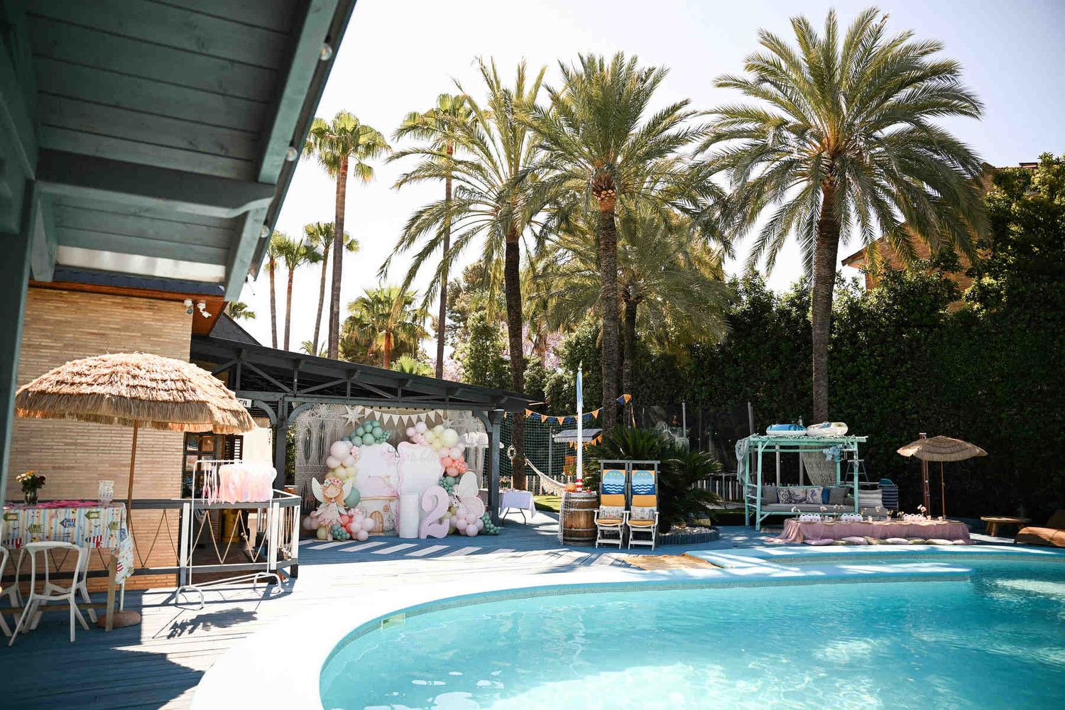 Resort-style outdoor birthday party venue in Valencia featuring a swimming pool, palm trees, and a themed balloon photo zone.