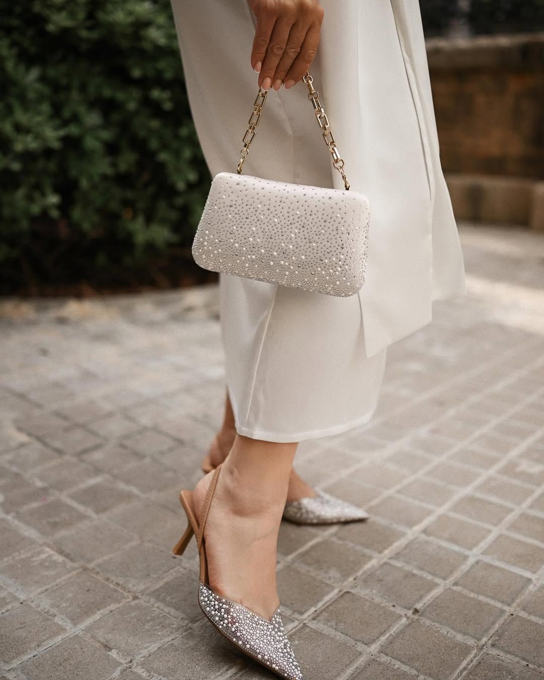 Close-up detail shot of silver sparkling shoes and a pearl clutch bag worn by a woman during a Valencia portrait session.