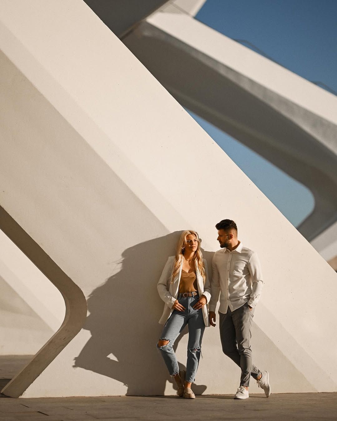 Modern engagement photography of a stylish couple standing against the geometric white concrete walls with sharp shadows