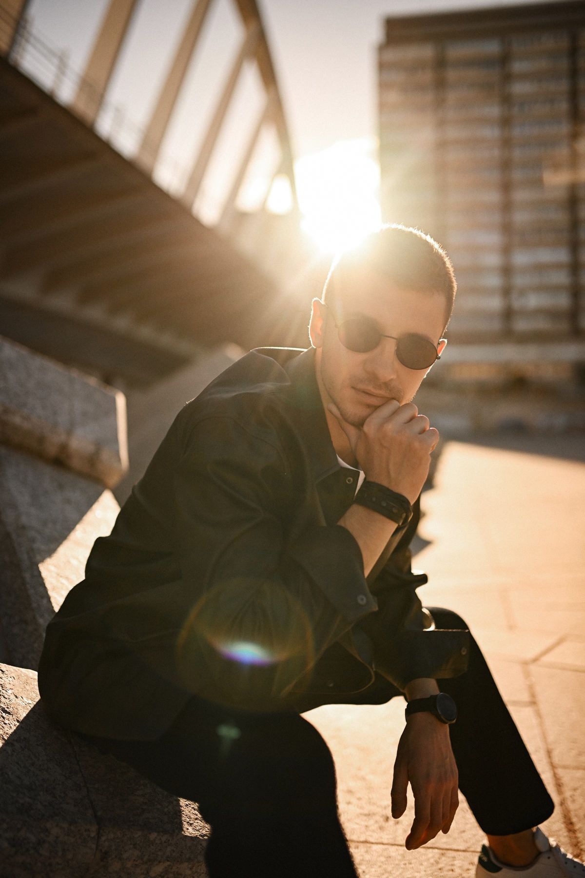 Cinematic portrait of a man in a leather jacket and sunglasses with a warm sun flare, looking directly into the camera.