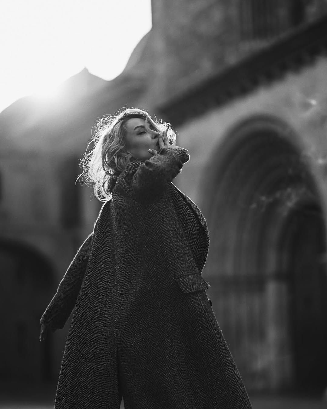 A dramatic black and white portrait of a model walking past historic old town architecture during a female fashion photoshoot.