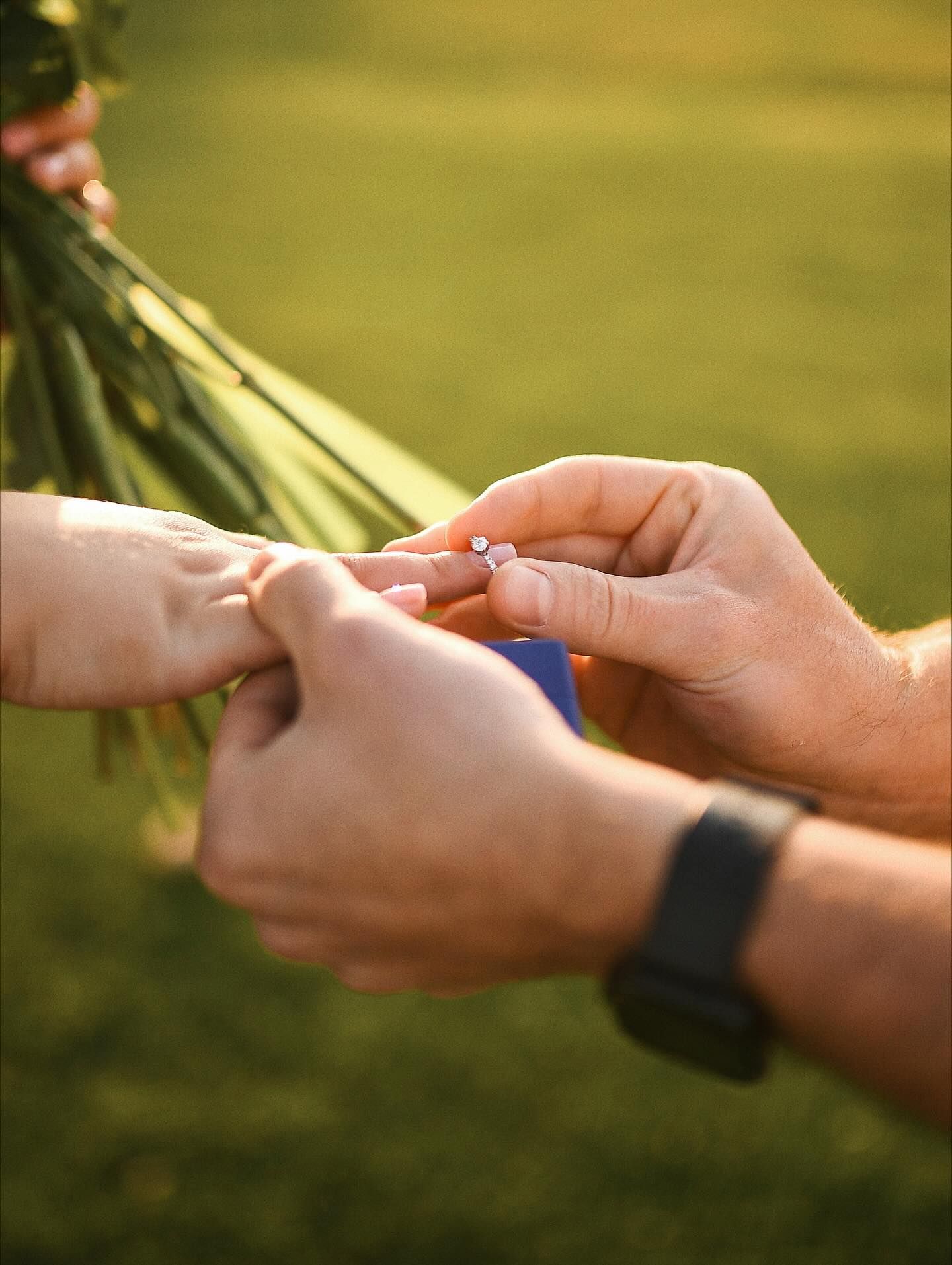 Close-up shot of a man's hands placing a delicate diamond engagement ring onto his partner's finger during a marriage proposal.