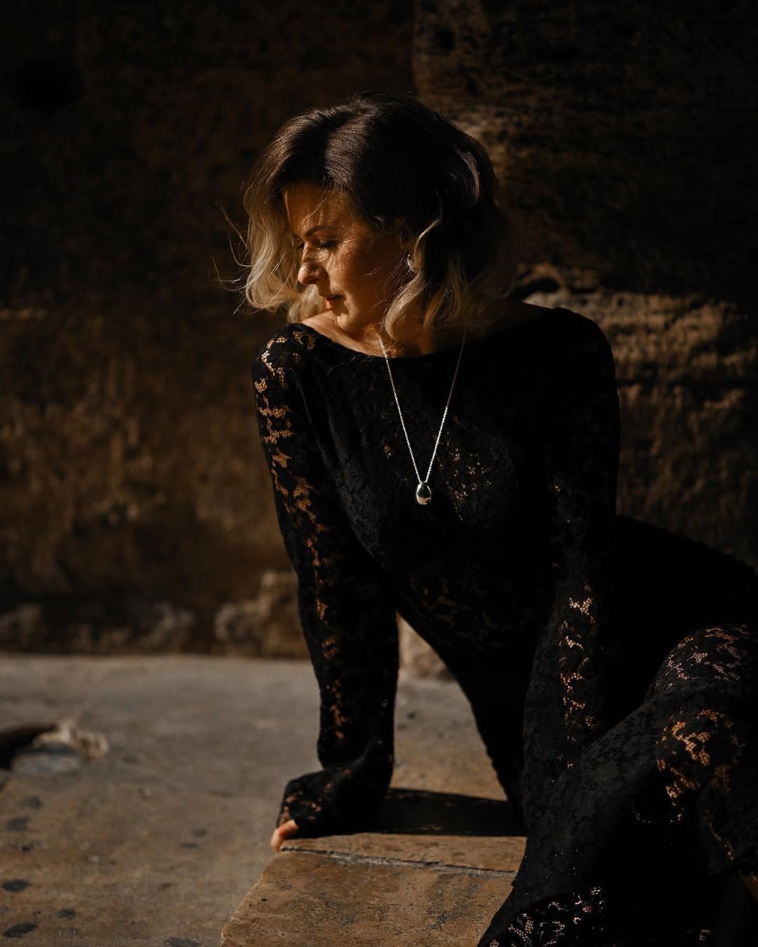 An editorial portrait of a woman leaning against a stone wall, showcasing professional hair and makeup from an all-inclusive session.