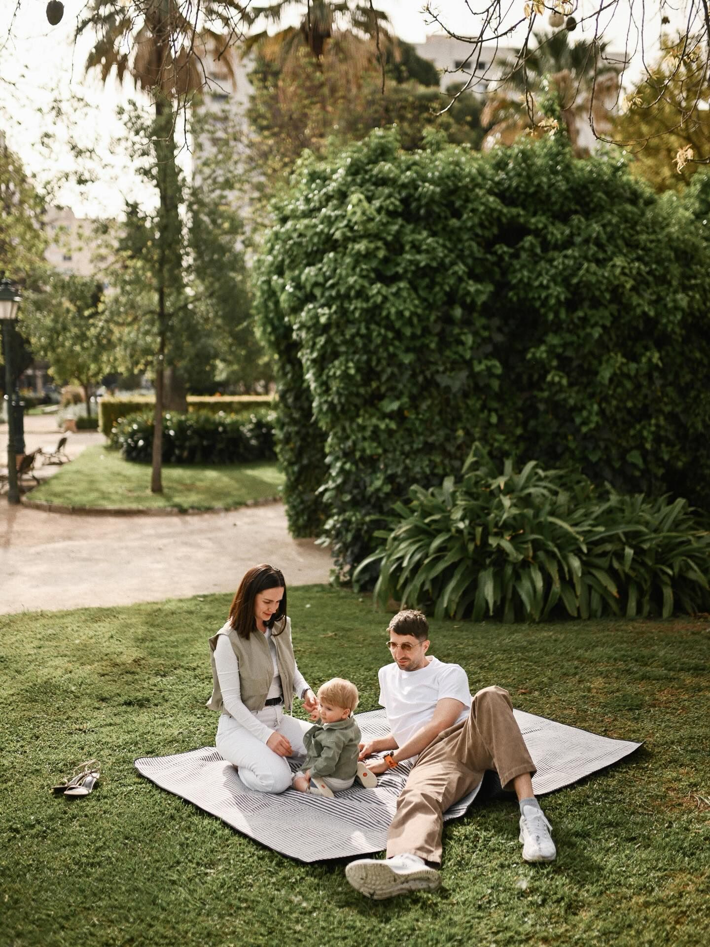 Parents sitting on a striped blanket on the grass with their baby boy during a casual outdoor family picnic session in Valencia.