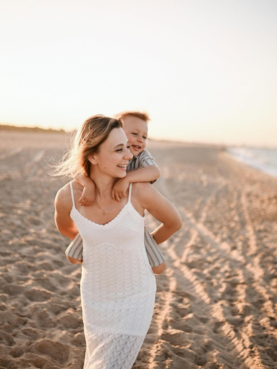 A mother gives her son a joyful piggyback ride across the warm sand during an afternoon family session at El Saler.