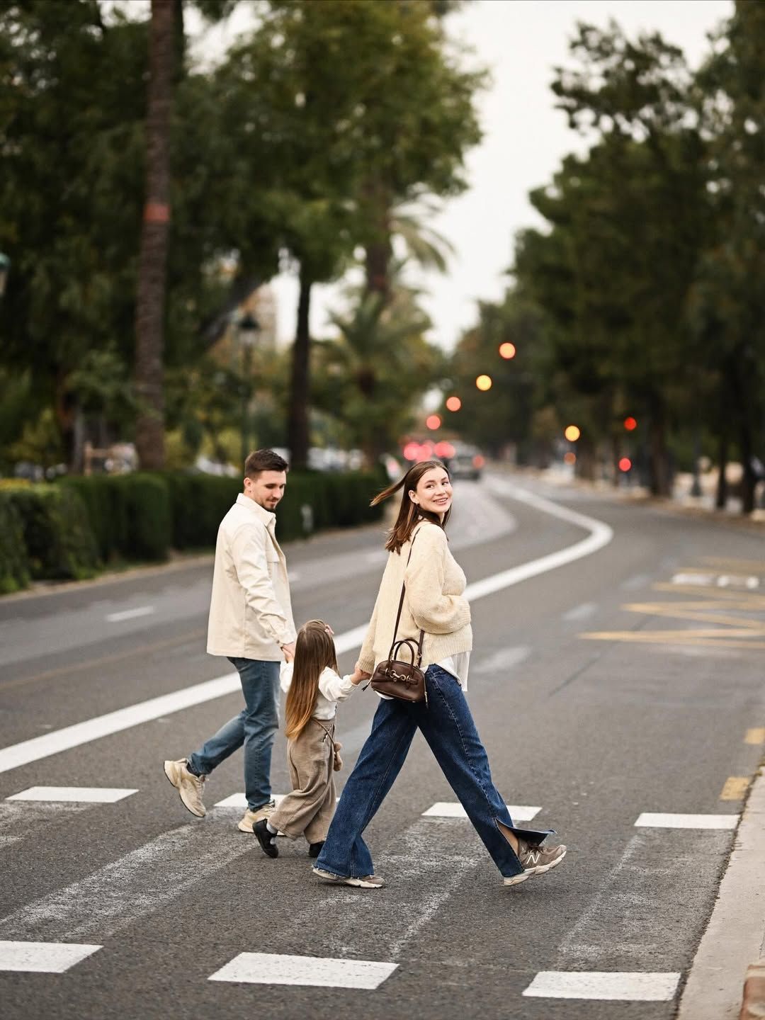 Parents expecting a baby and their daughter crossing a quiet street beside Turia Park in Valencia during an evening maternity session.