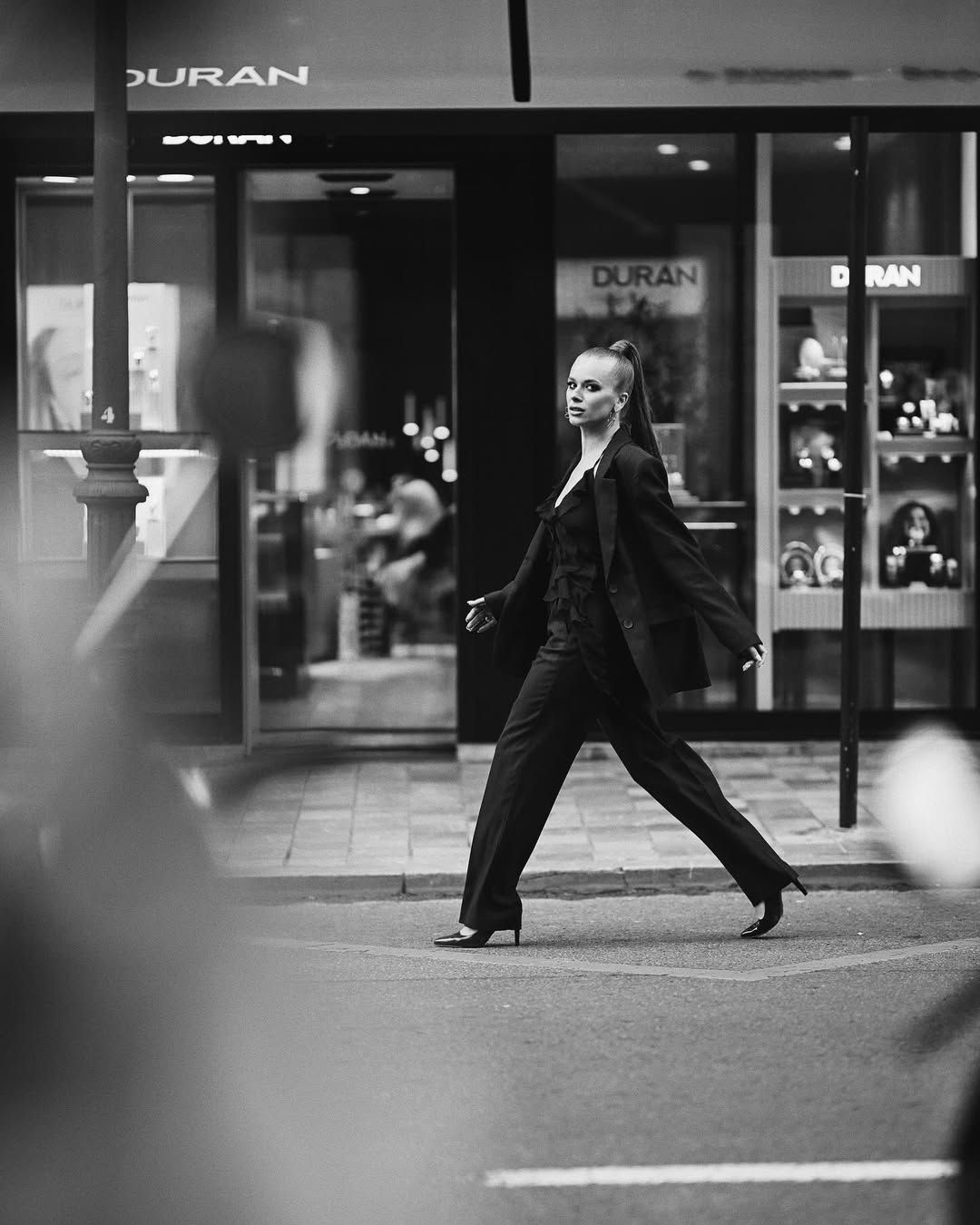 A full-length black and white fashion photograph of a model walking confidently through the streets of Valencia.