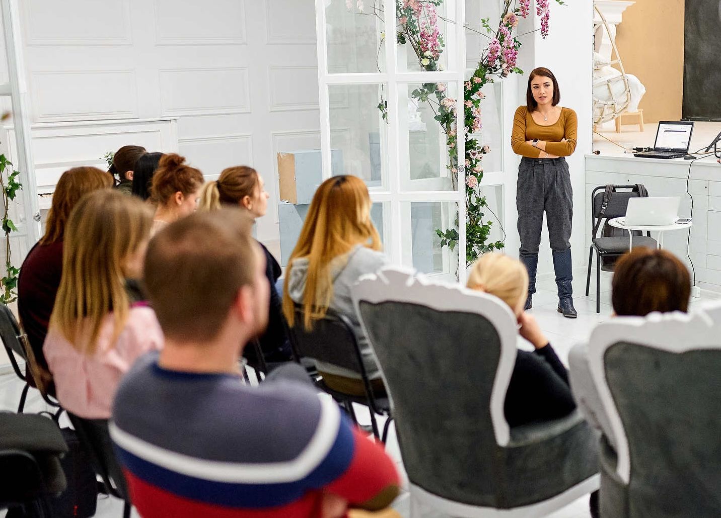Professional photography workshop with a female speaker educating a seated group of photographers in a bright studio setting.