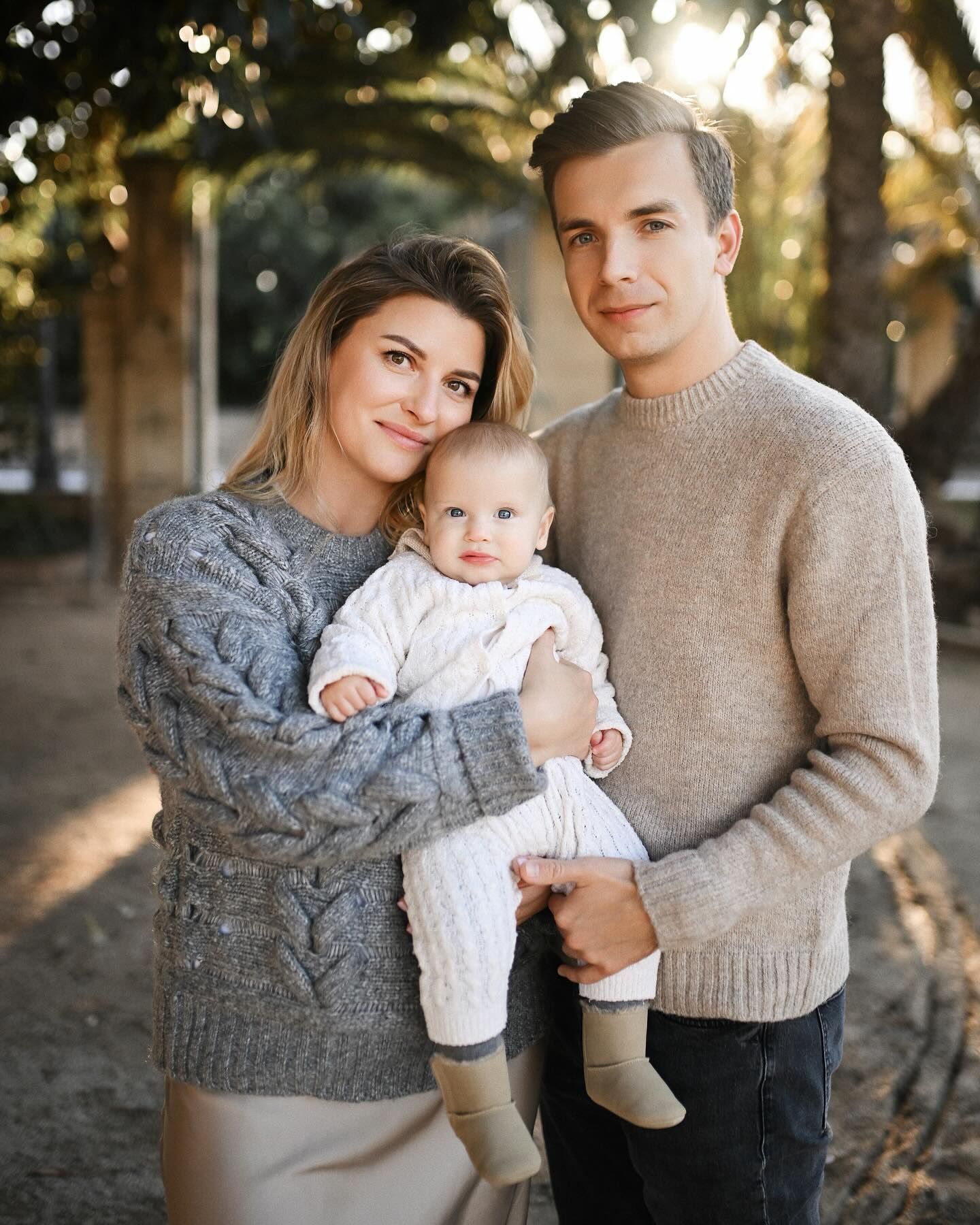 Three-quarter portrait of a mother, father, and their little baby in white knitwear during a lifestyle baby session in Valencia.