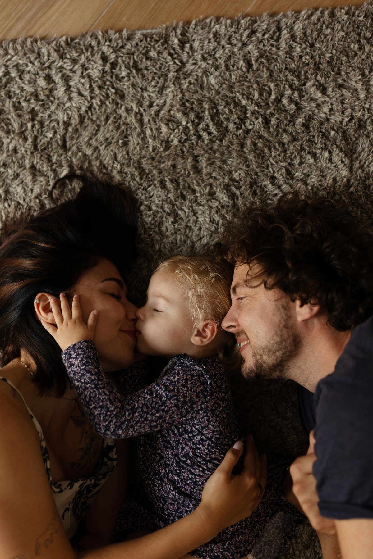 Intimate family portrait of photographers Yuri and Darina Derzkaya lying down on a cozy rug with their young daughter.
