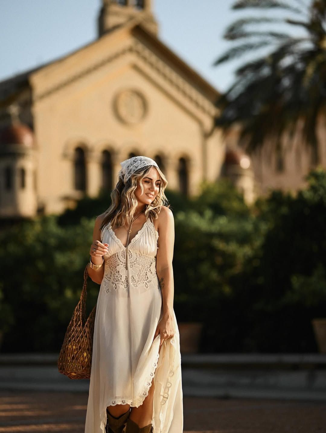 Smiling woman walking through Jardín de Las Hespérides holding a bag of lemons with a classic Valencia building behind her