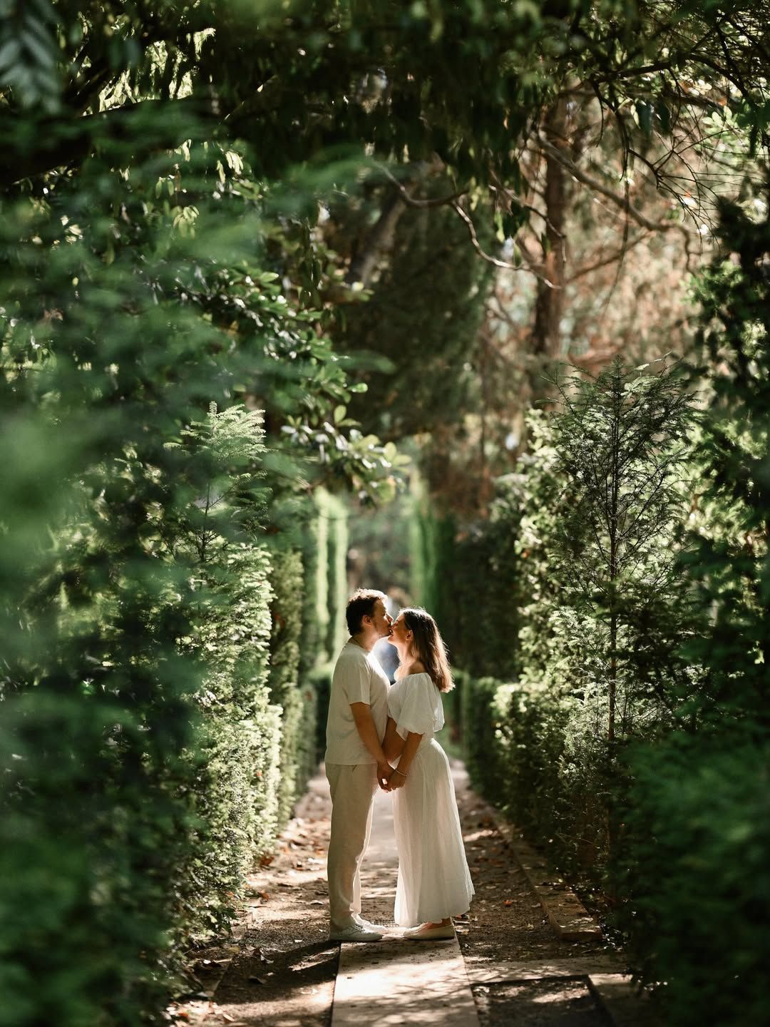 Expecting couple kissing in a manicured hedge tunnel with beautiful morning backlight at Jardines de Monforte in Valencia