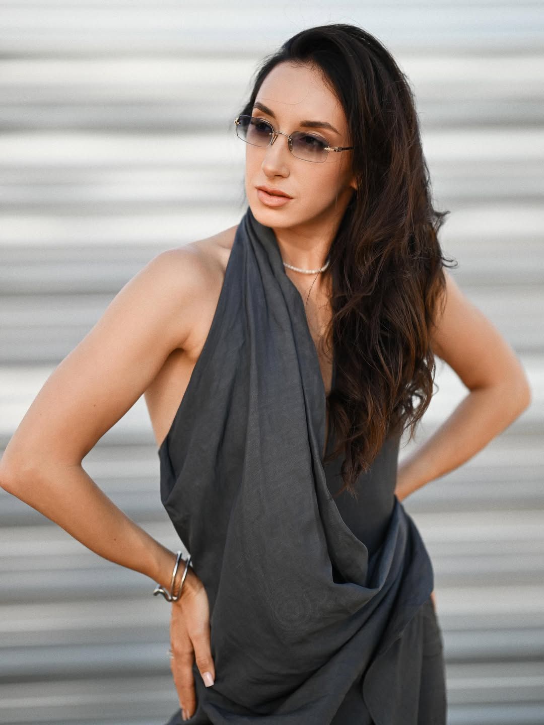 Stylish woman wearing sunglasses and a dark dress posing against a modern textured wall during a Valencia photoshoot.
