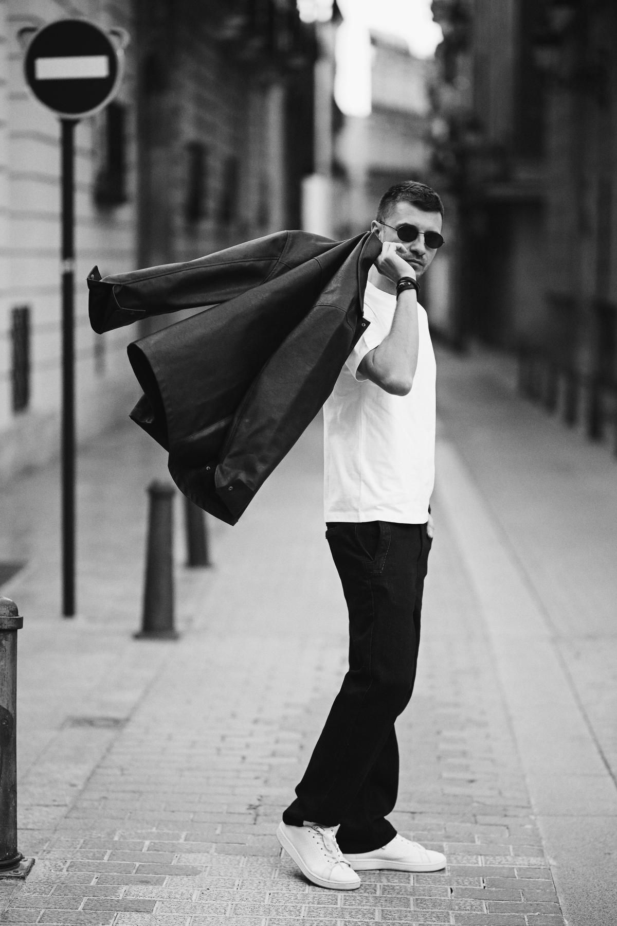 Dynamic candid photo of a man tossing a leather jacket over his shoulder while walking through the streets of Valencia.