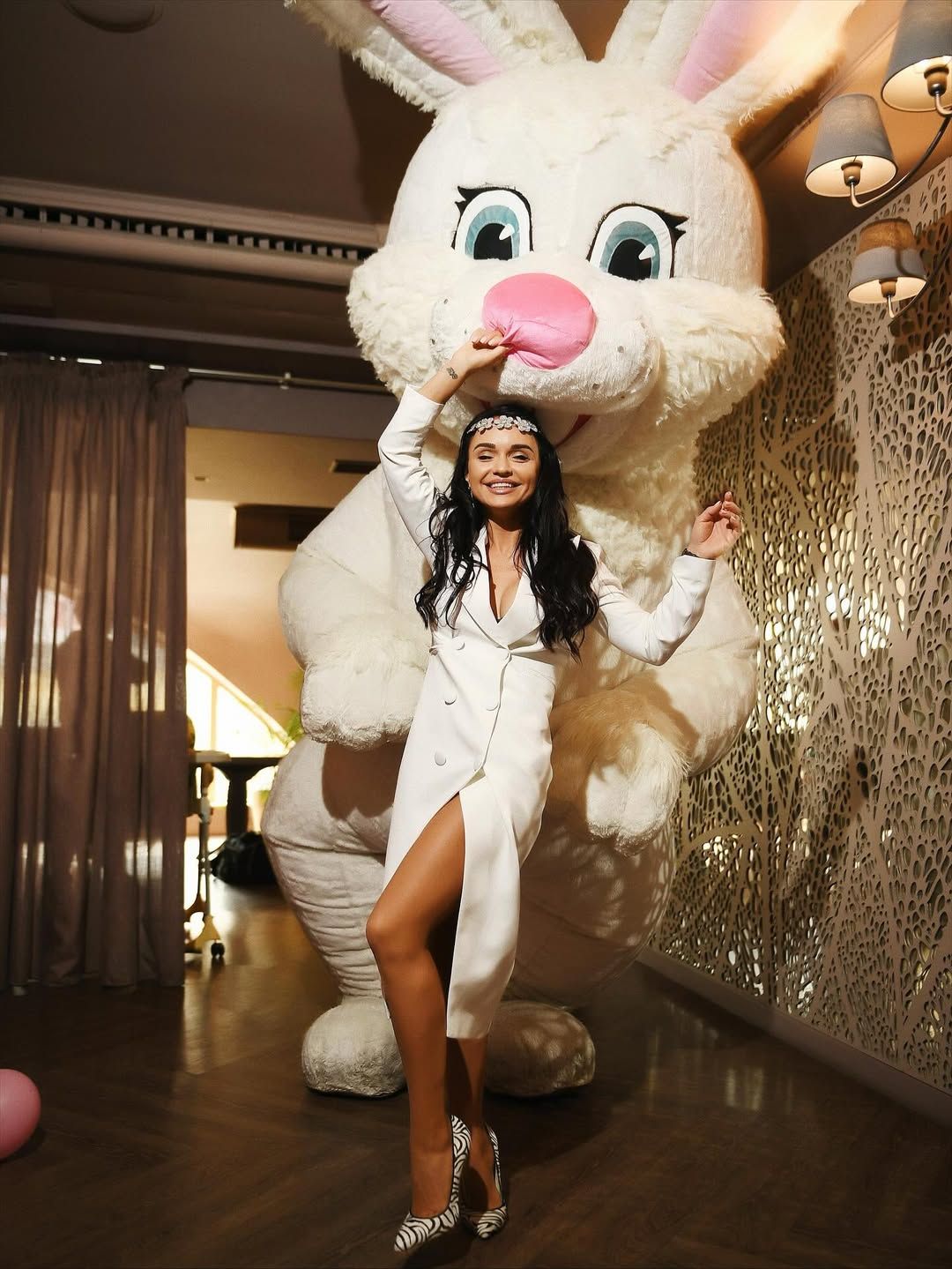 Elegant mother smiling and posing in front of a giant plush bunny animator during a children's show program.