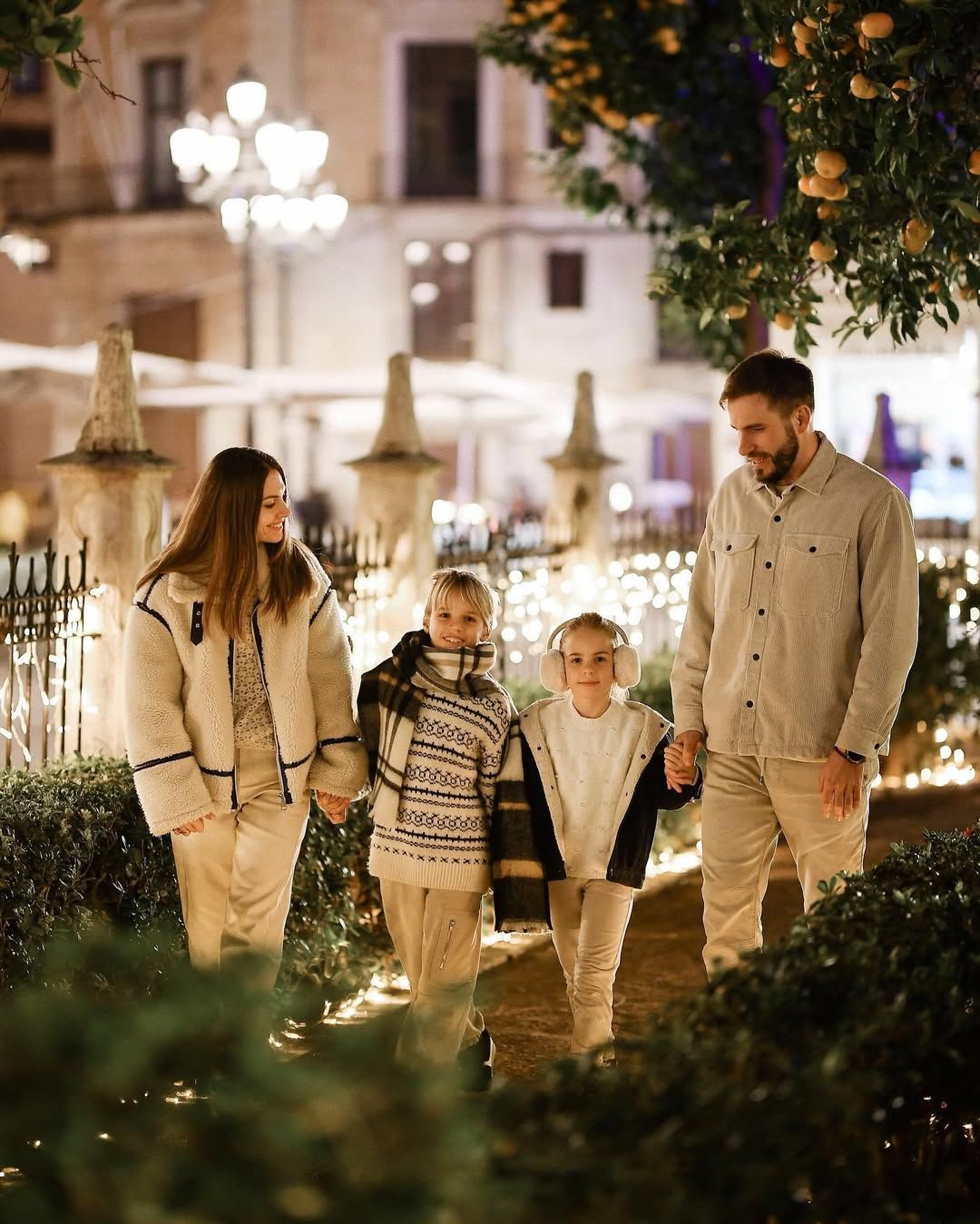 Family walking together along a path lined with fairy lights and Valencia orange trees during a cozy holiday photoshoot