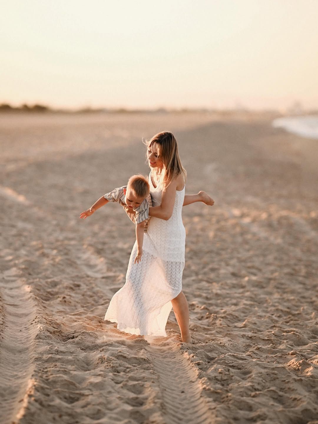 Mother playfully lifting her boy like an airplane on the soft sand during a sunset session at El Saler beach.