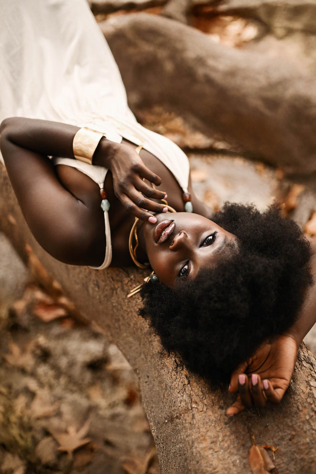 Moody overhead shot of a model lying gracefully across a massive, textured tree root for a fine art portrait gallery.