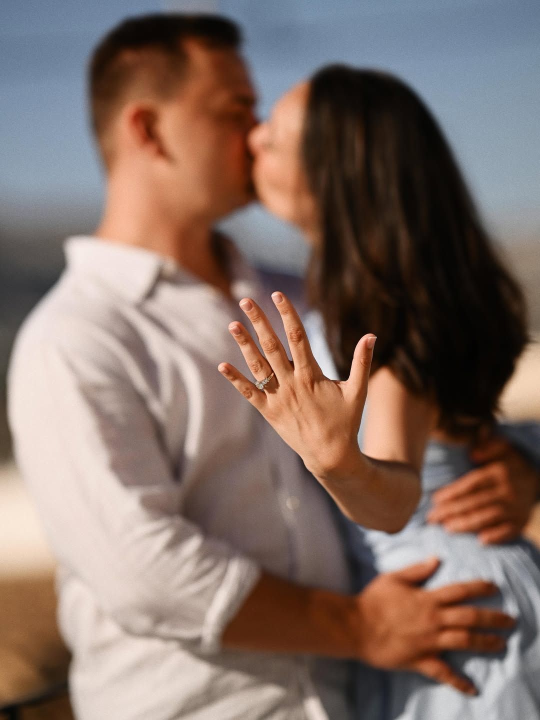 An engaged couple kissing after the successful proposal, with the bride proudly showing off her new diamond engagement ring to the camera.