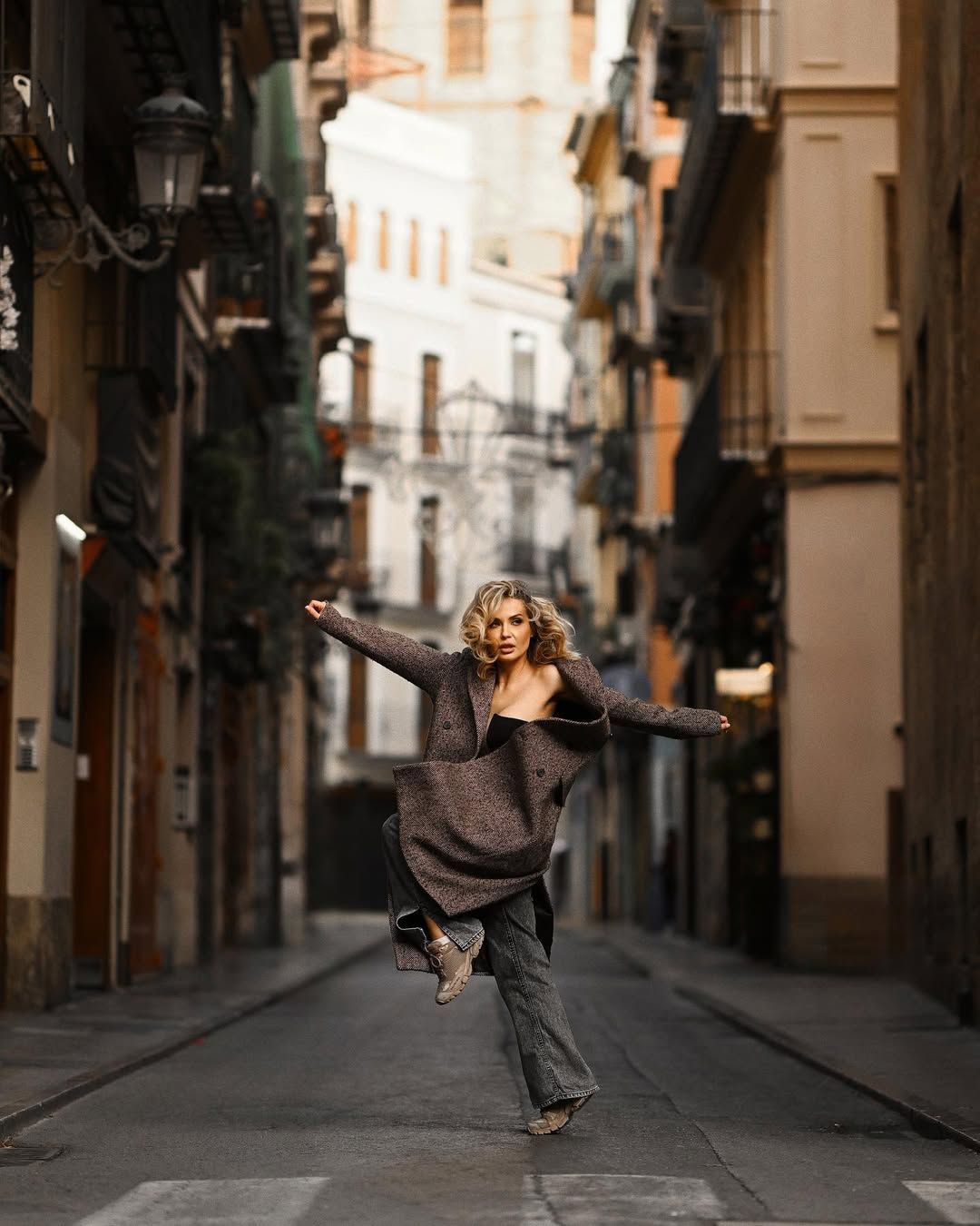 A model moves dynamically down an empty historic street, showcasing her outfit for a high-fashion portrait session in Valencia.