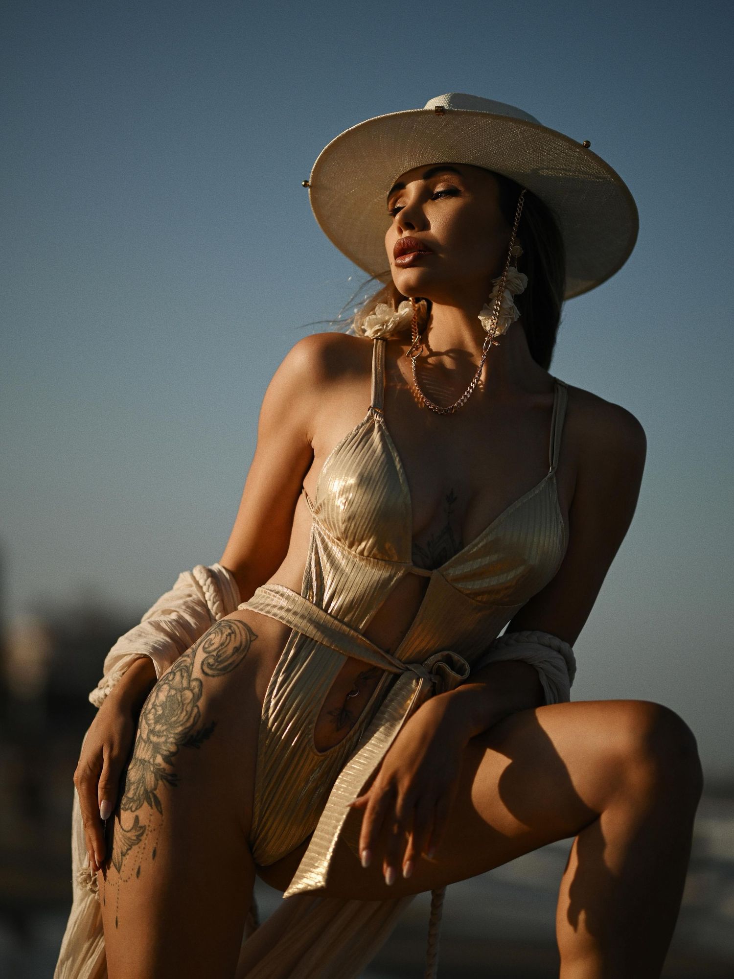 An editorial portrait of a woman in a wide straw hat posing under the warm evening sun during a beach photo session.
