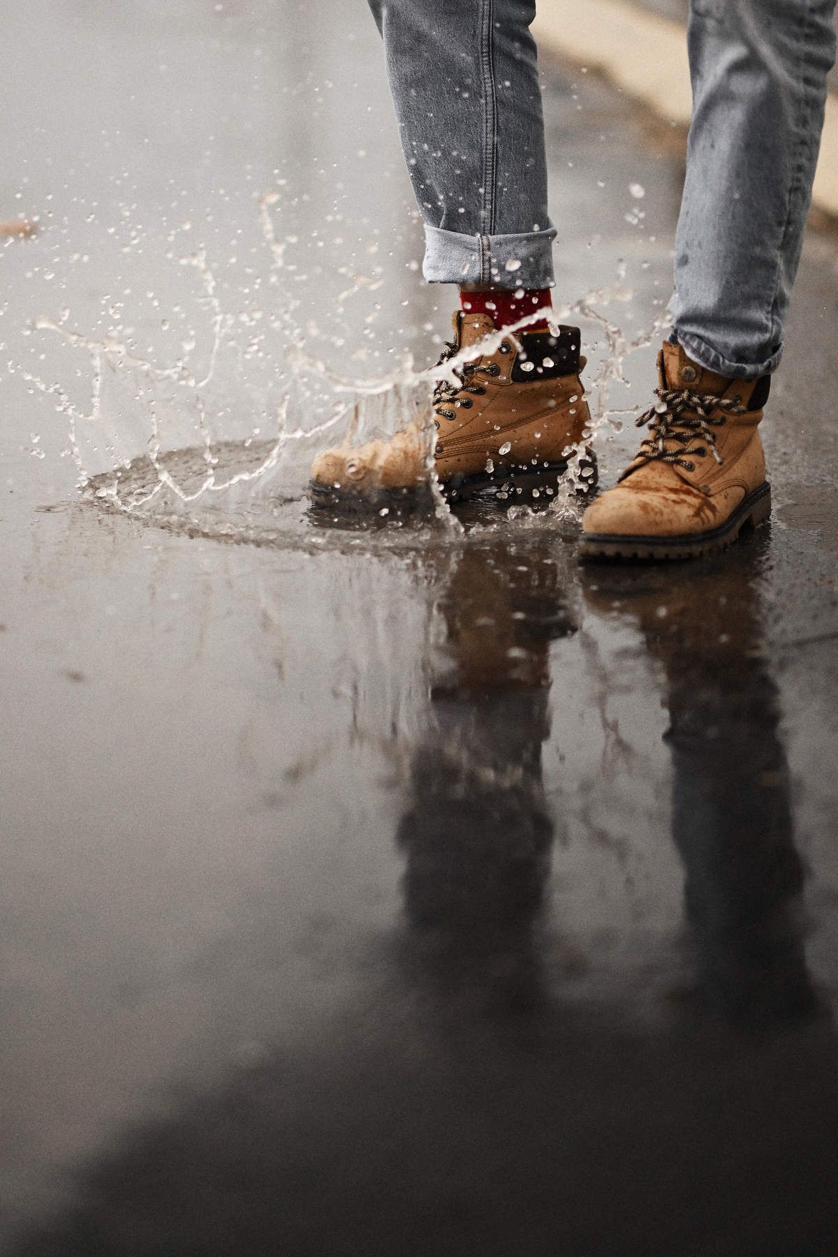 Close-up of men's classic leather boots splashing into a puddle in Valencia city center, capturing a dynamic documentary vibe.