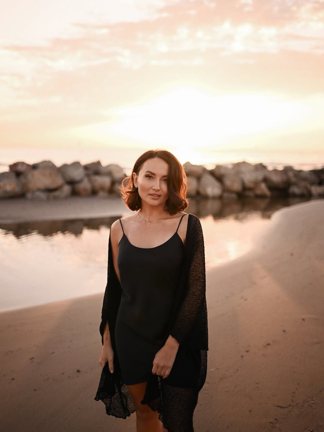 Female beach photoshoot in Valencia, featuring a woman standing near a tidal pool with the sunset reflecting on the calm water.