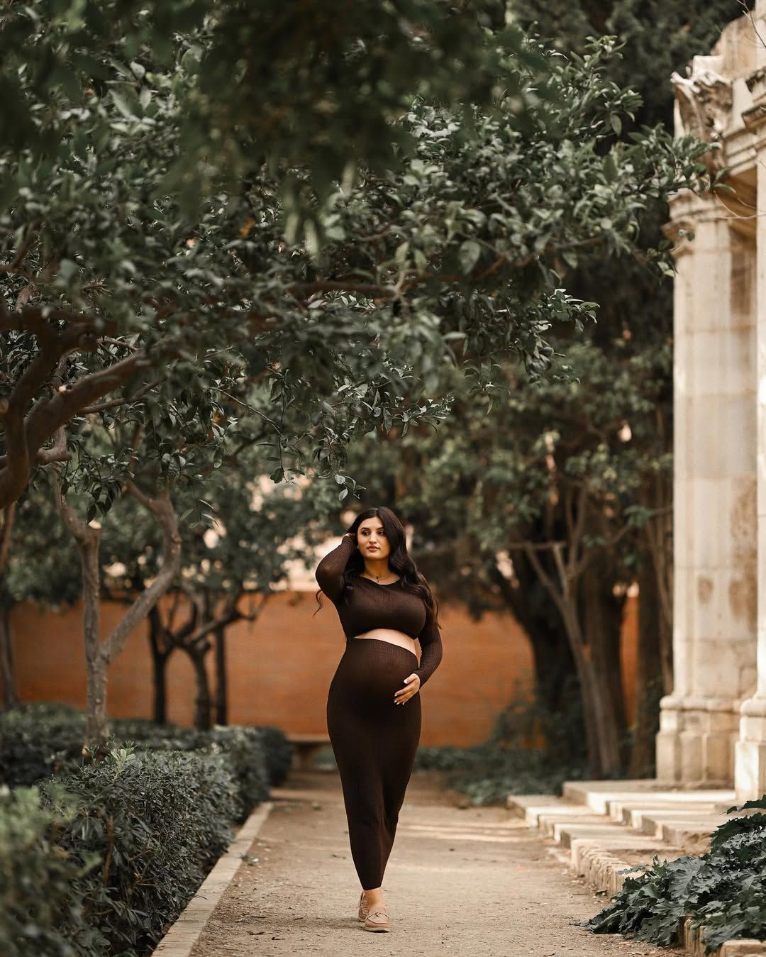 Pregnant woman walking on a park pathway under the deep shade of green trees in Jardines del Real, Valencia