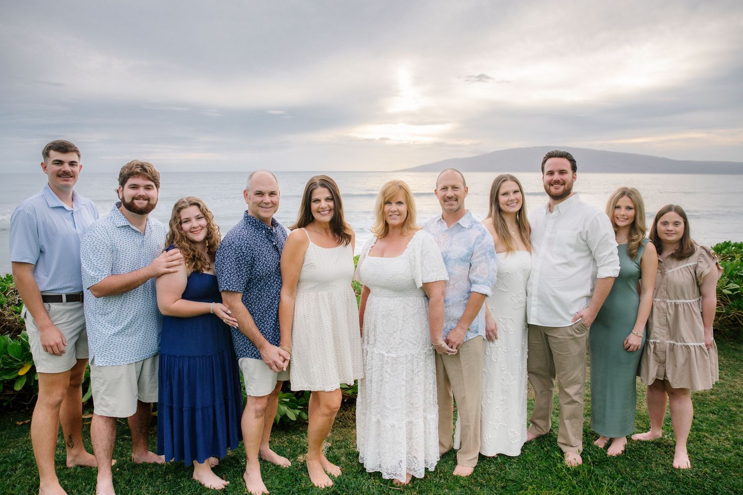 Group portrait of family members in coordinated outfits against ocean backdrop.