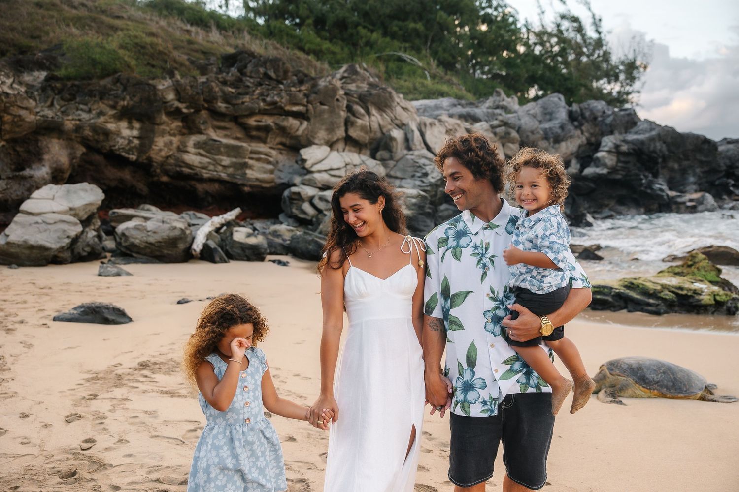 A group poses together on a rocky beach shoreline during golden hour.