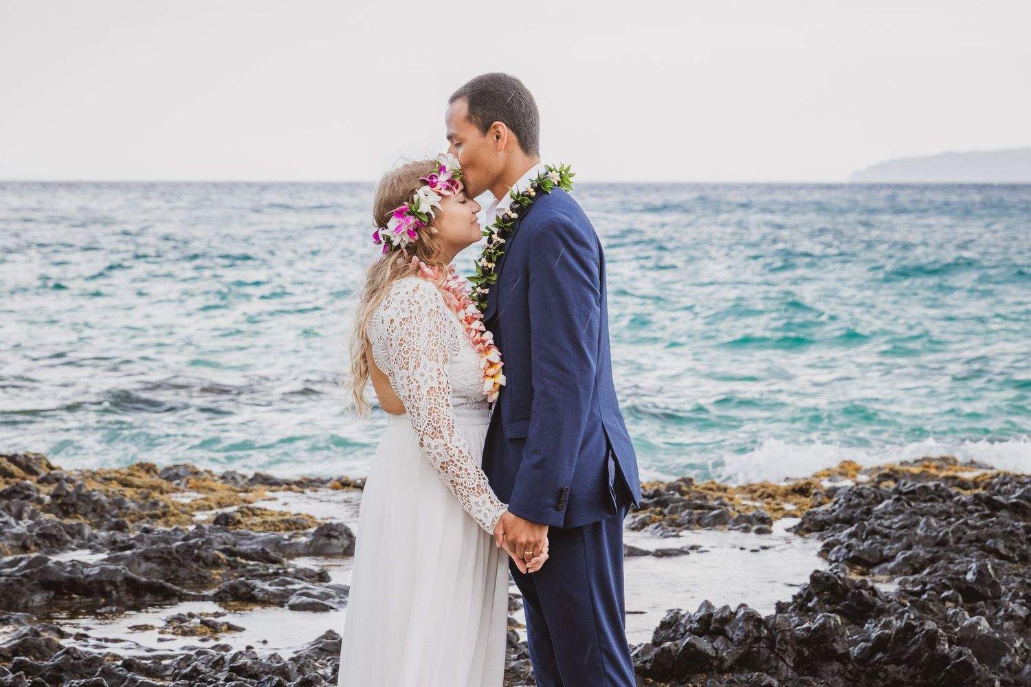 Romantic beach wedding scene with turquoise ocean and volcanic rocks in the background.