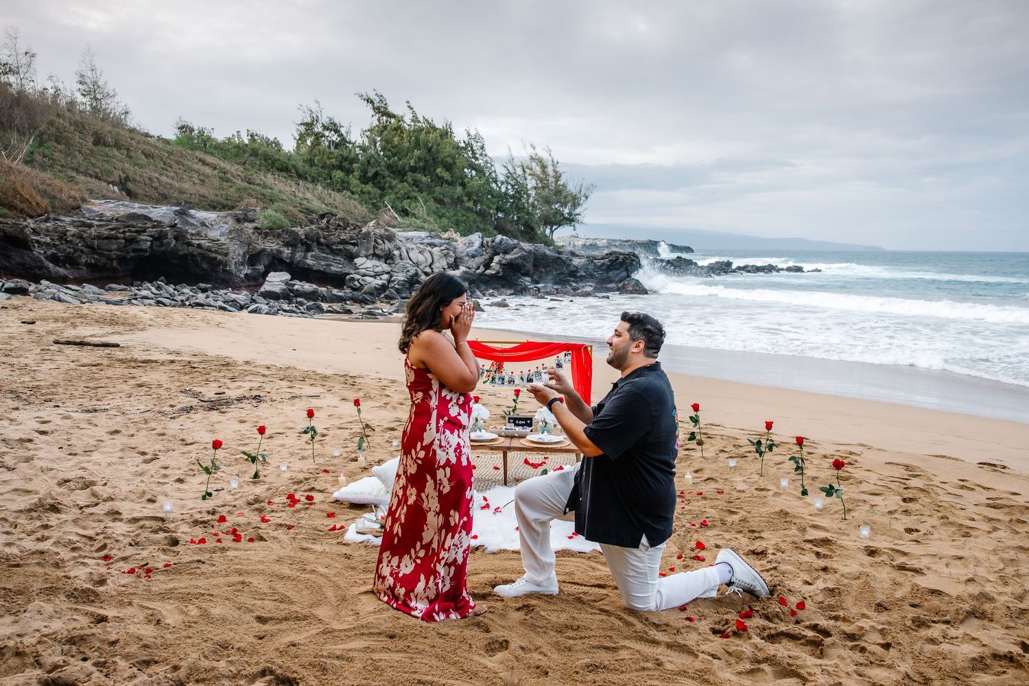 Romantic beach proposal scene with rose petals arranged on sandy shoreline.