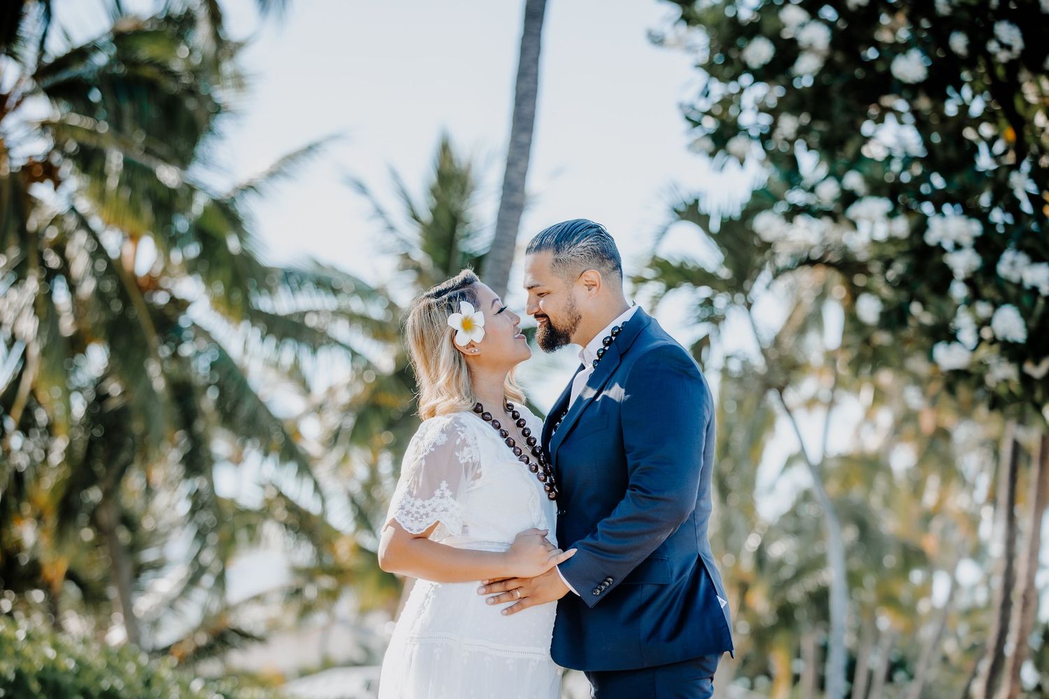Bride and groom share a romantic kiss surrounded by tropical palm trees at their outdoor beach wedding.